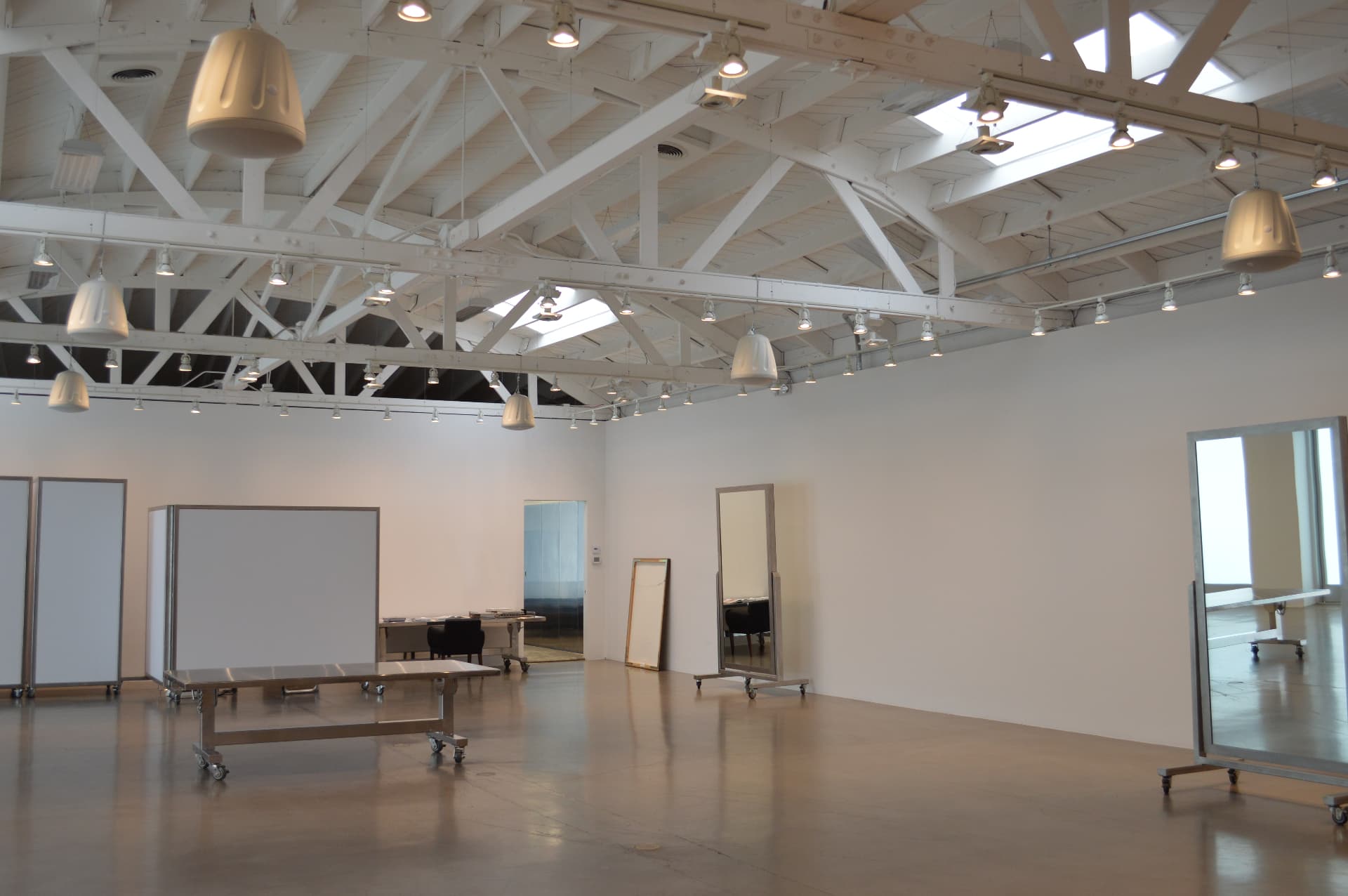 Commercial AV installation in a large open showroom with exposed beams, distributed track lighting, and ceiling-mounted speakers.