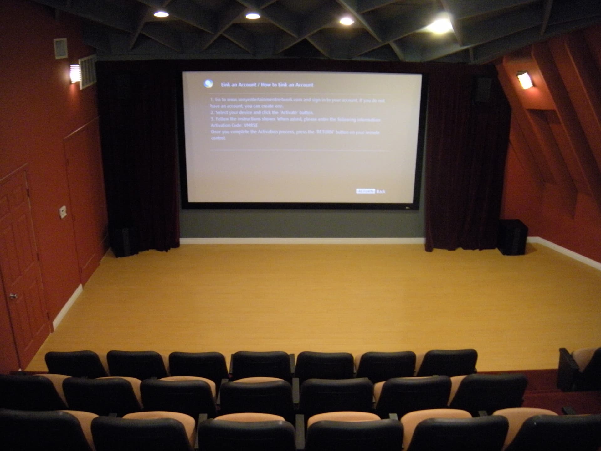 Commercial theater installation with ceiling acoustic treatment, wall speakers, and a large projection display.