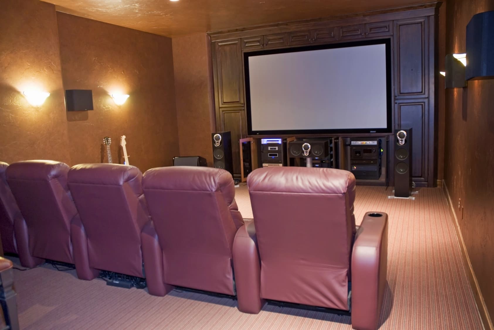 Luxury home theater with leather recliners, floor-standing speakers, and framed projection screen with warm ambient lighting