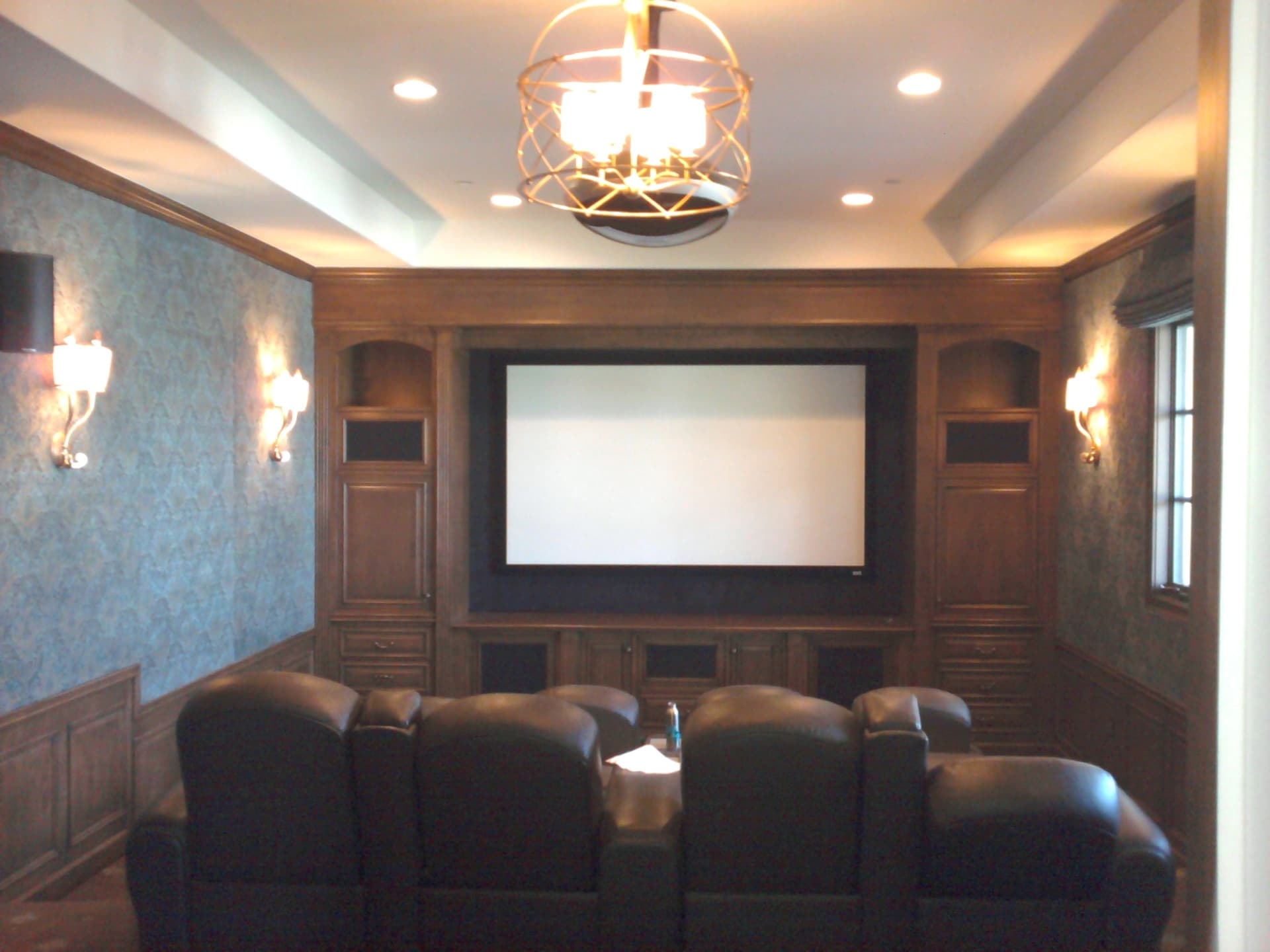 Elegant dedicated theater room with custom millwork, projection screen, and plush leather seating