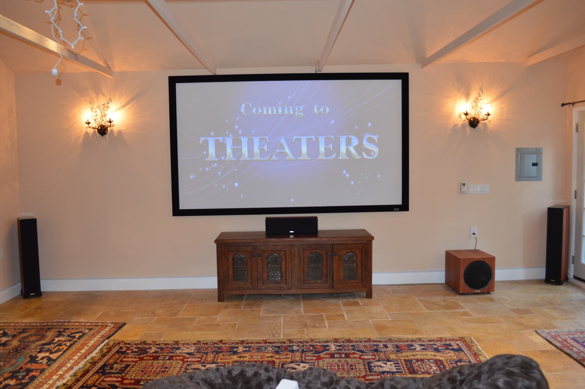 Rustic home theater with projection screen, media cabinet, and floor-standing speakers with decorative sconces