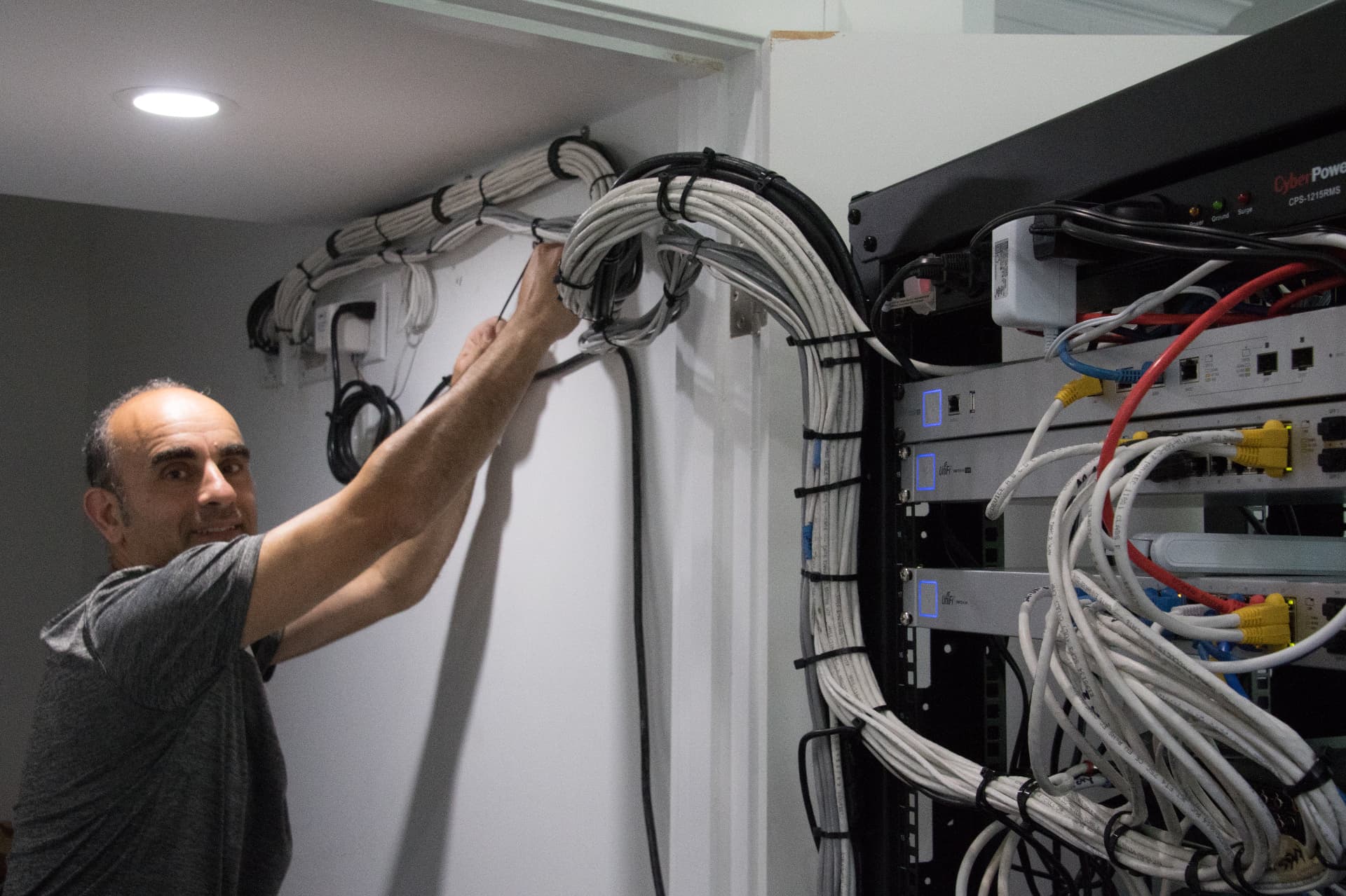 Ron securing a large bundle of labeled low-voltage cables along the wall into a structured network rack
