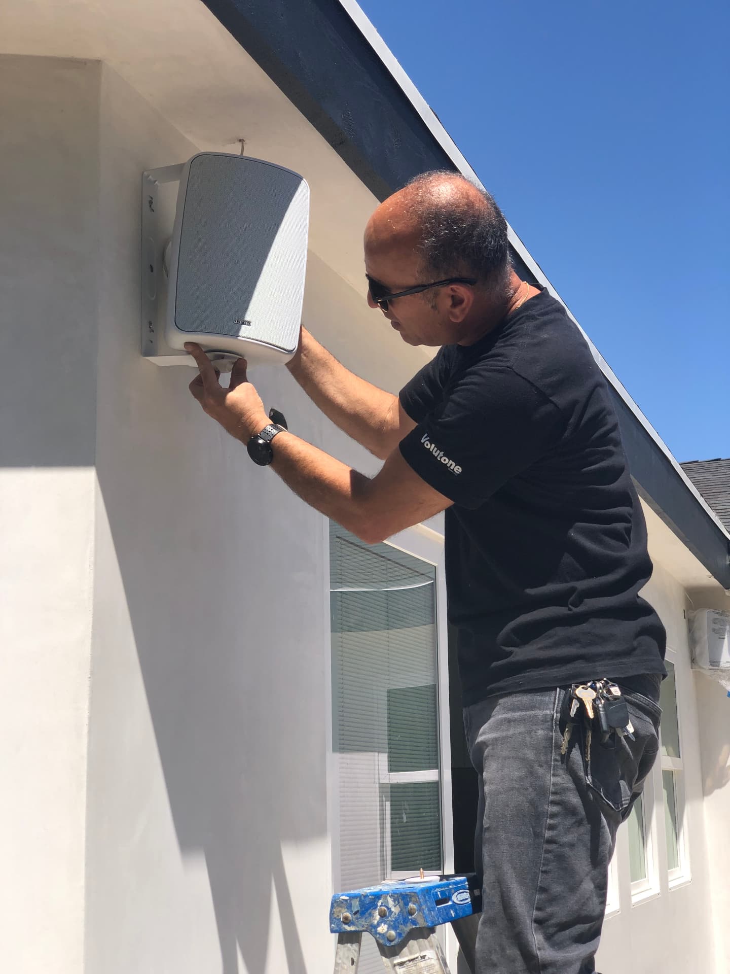 Technician installing weatherproof outdoor speaker on exterior wall for whole-home audio coverage