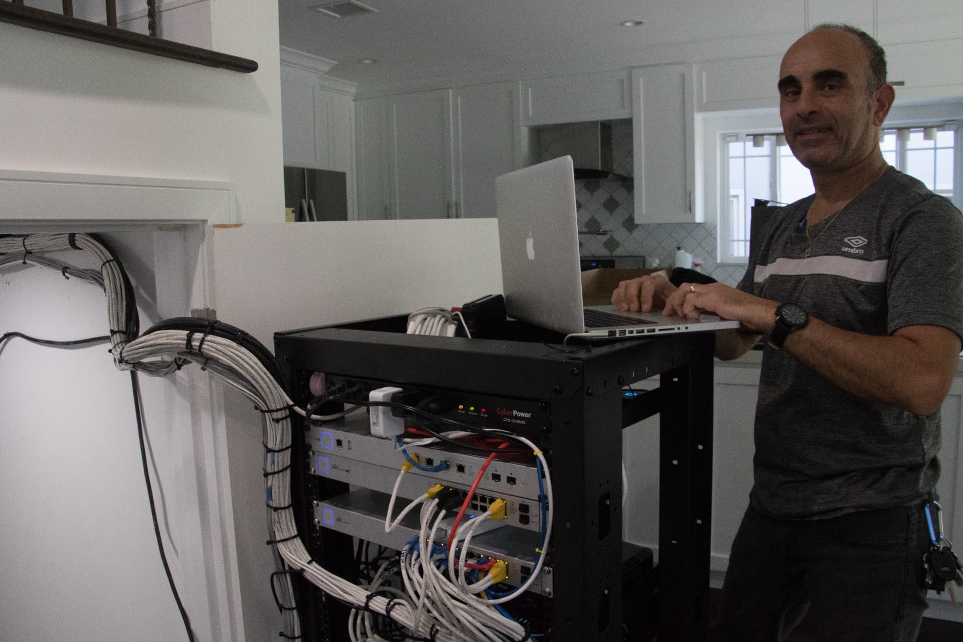 Technician configuring a home network rack using a laptop on a rolling AV cabinet