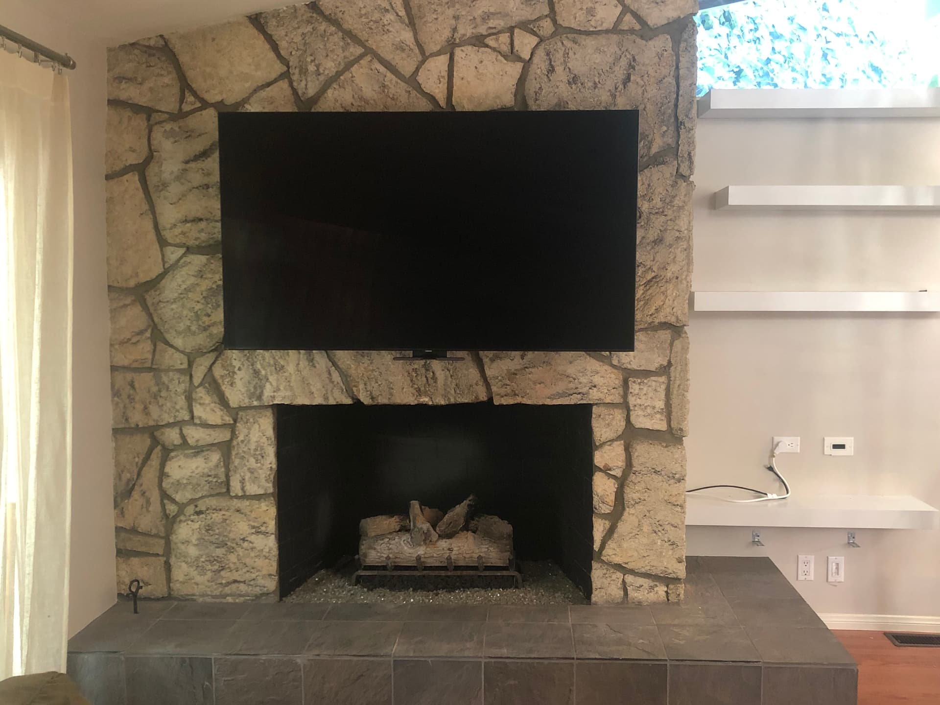 TV mounted on natural stone fireplace in modern living room with clean cable concealment