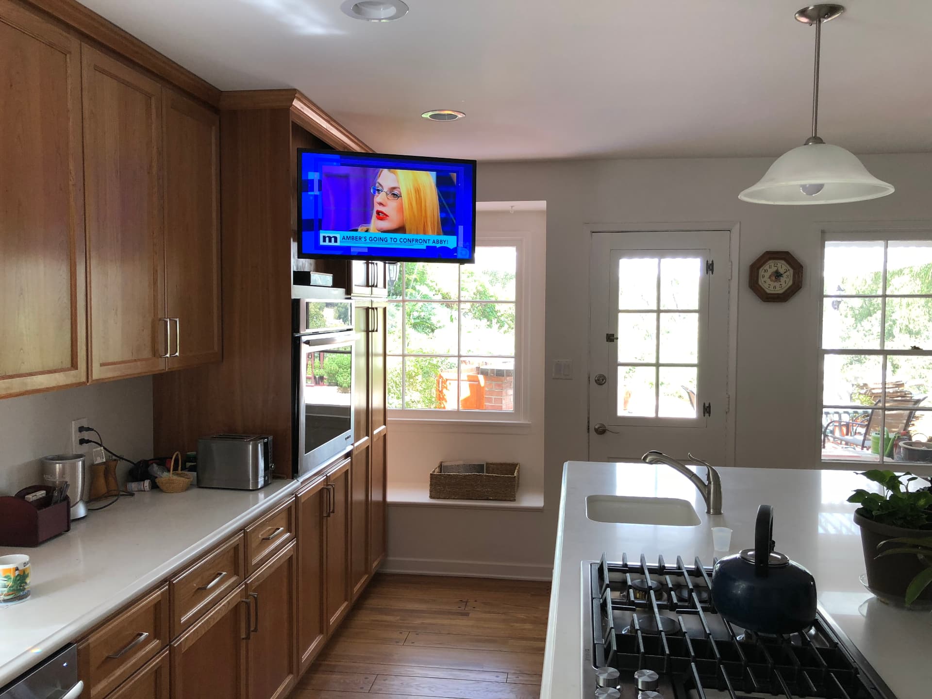 Small TV mounted in bright kitchen above built-in oven with in-ceiling speakers