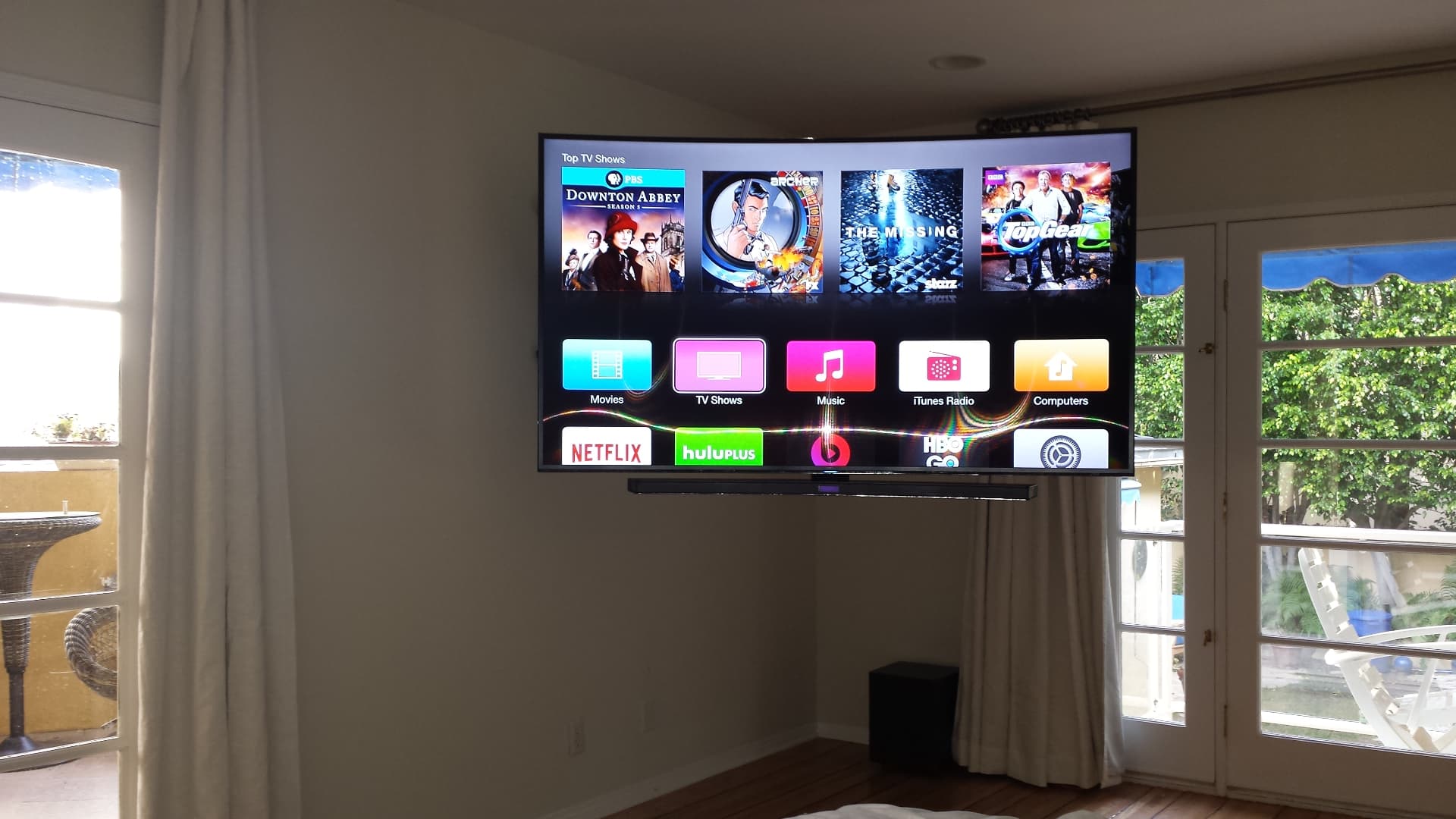 Curved Samsung TV corner-mounted in bright room with soundbar and streaming interface