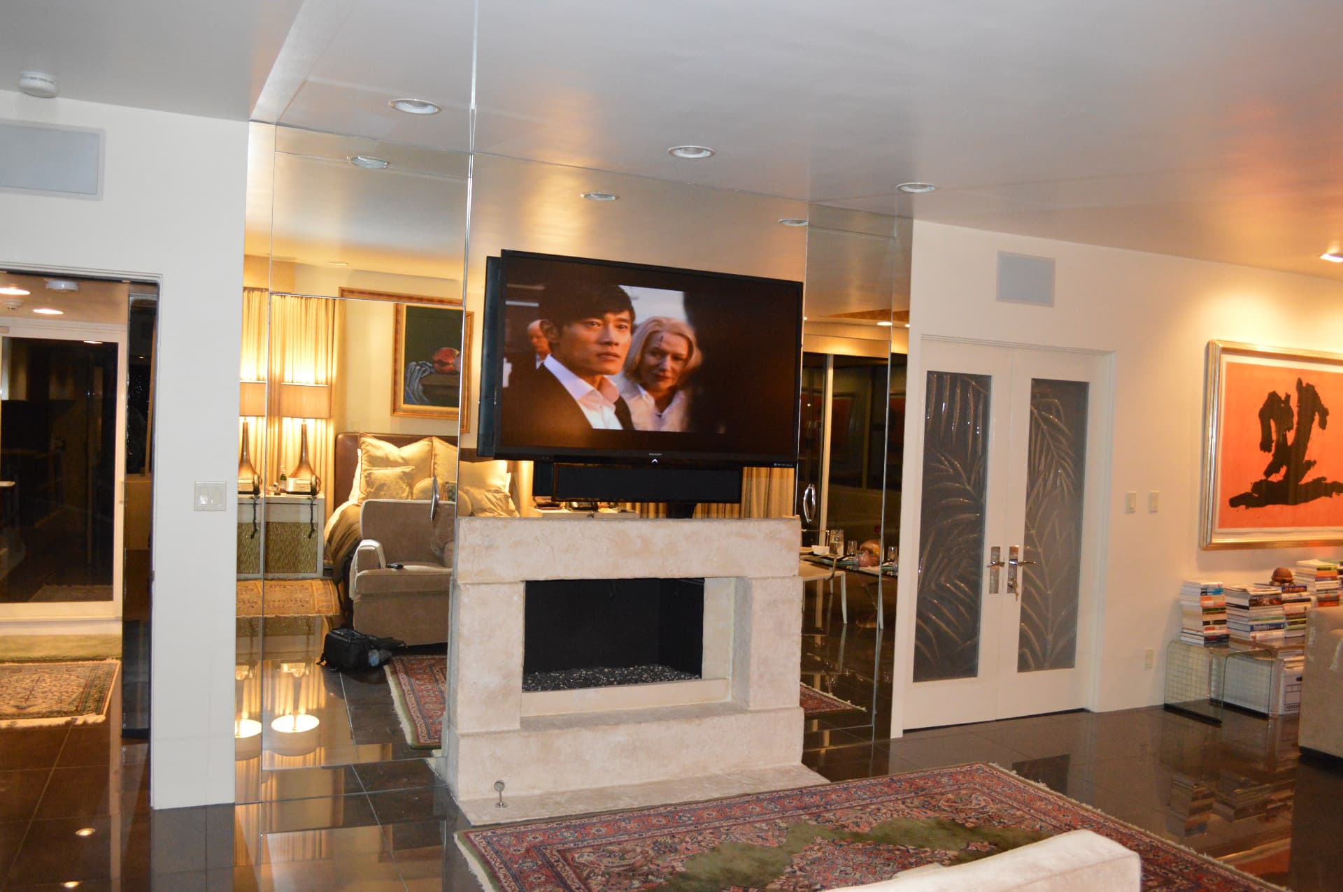 TV on modern fireplace mantel in upscale living room with mirrored walls and art