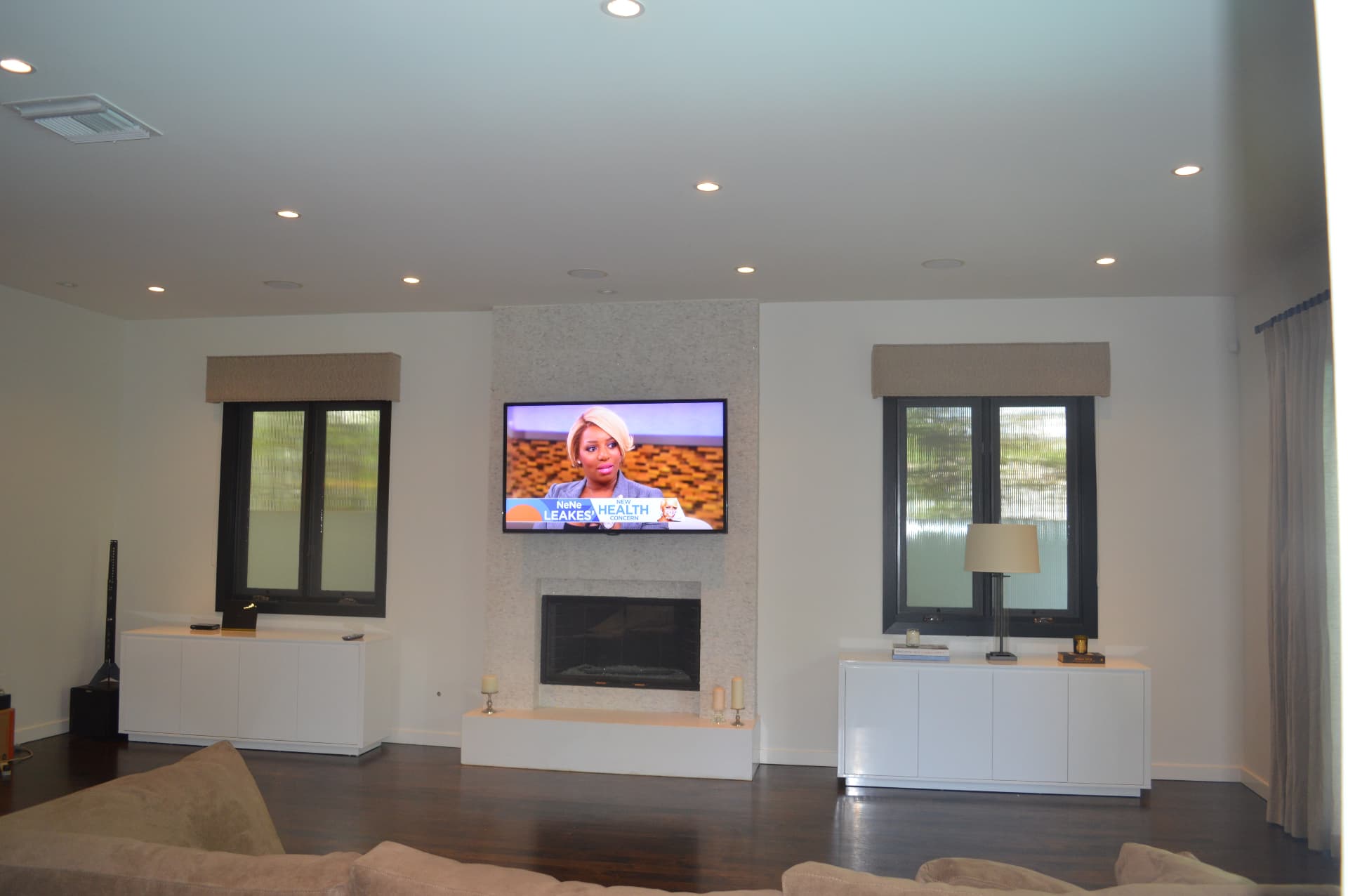 Large TV above white stone fireplace in contemporary living room with in-ceiling speakers
